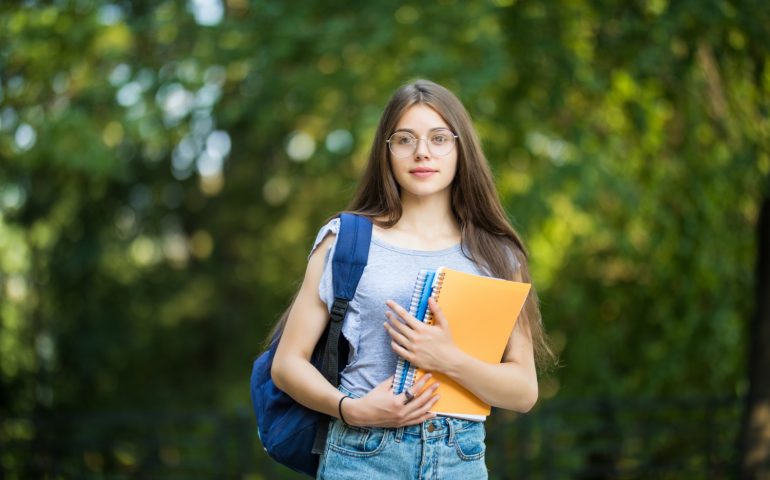 cheerful-attractive-young-woman-with-backpack-notebooks-standing-smiling-park